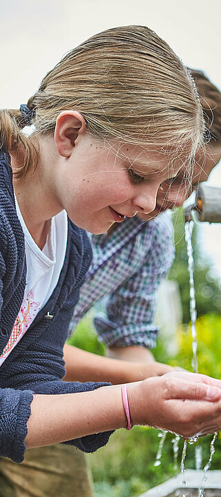 ein Mädchen und ein Junge bei einem Trinkwasserbrunnen im Pinzgau